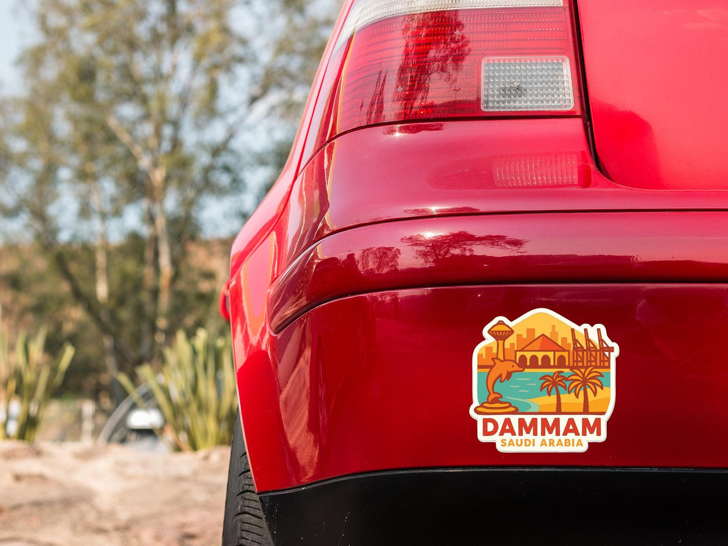 the rear end of a red car with a sticker on the trunk that says "DAMRAM SAUDI ARABIA".