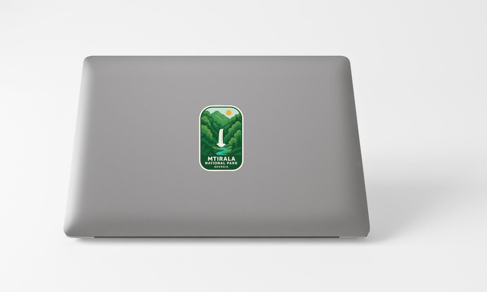 A sticker with a mountain landscape and the text "MTIRALA NATIONAL PARK" is placed on the back of a grey laptop computer.