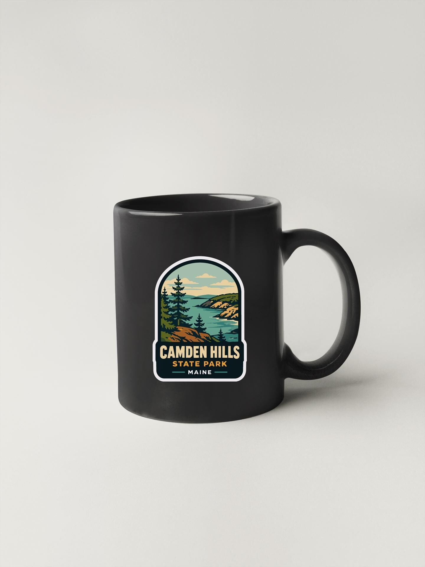 A black coffee mug with a sticker depicting a scenic landscape, including pine trees, mountains, and a body of water.