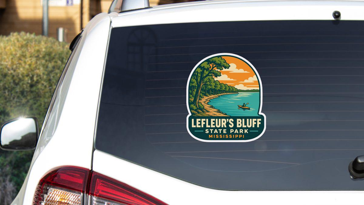A sticker on the rear window of a white vehicle, depicting a scenic landscape with a lake, trees, and a sunset.