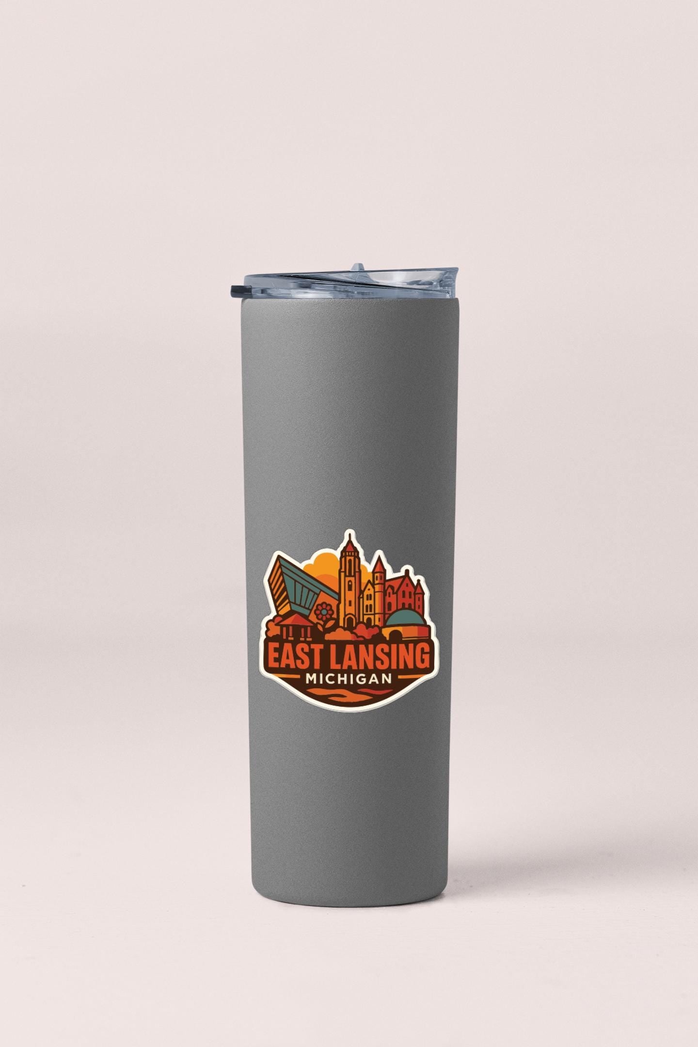 A gray insulated tumbler with a lid and a sticker featuring the text "EAST LANSING MICHIGAN" printed on it.