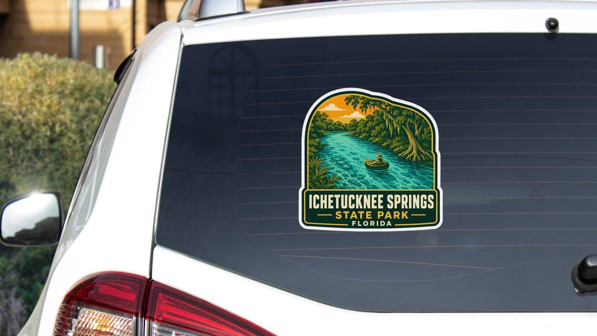 A sticker on the rear window of a white car, depicting a scenic landscape with a river and a boat, along with the text "ICETUCKNEES SPRINGS STATE PARK FLORIDA".