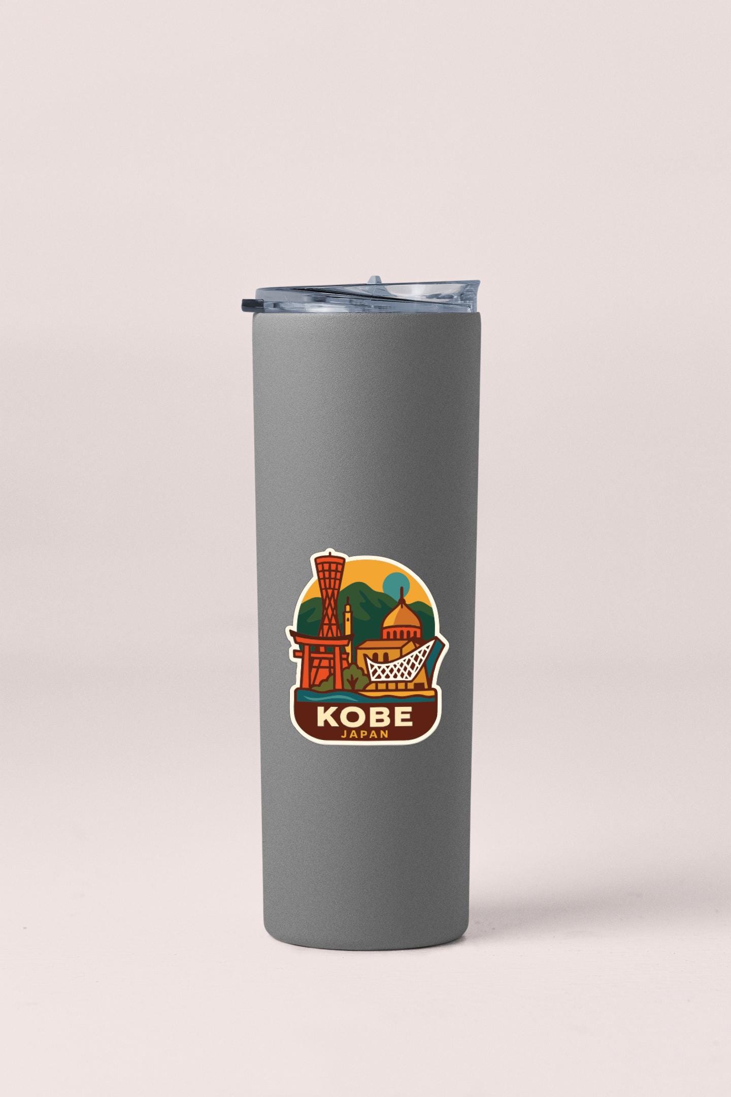 A gray insulated tumbler with a sticker depicting a cityscape and the word "Kobe" printed on it.