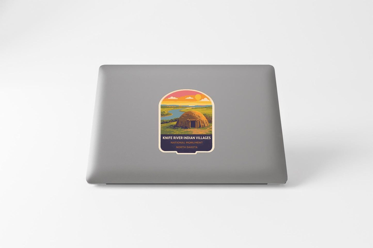 A sticker on the back of a laptop, depicting a scenic landscape with a hut or structure in the foreground.