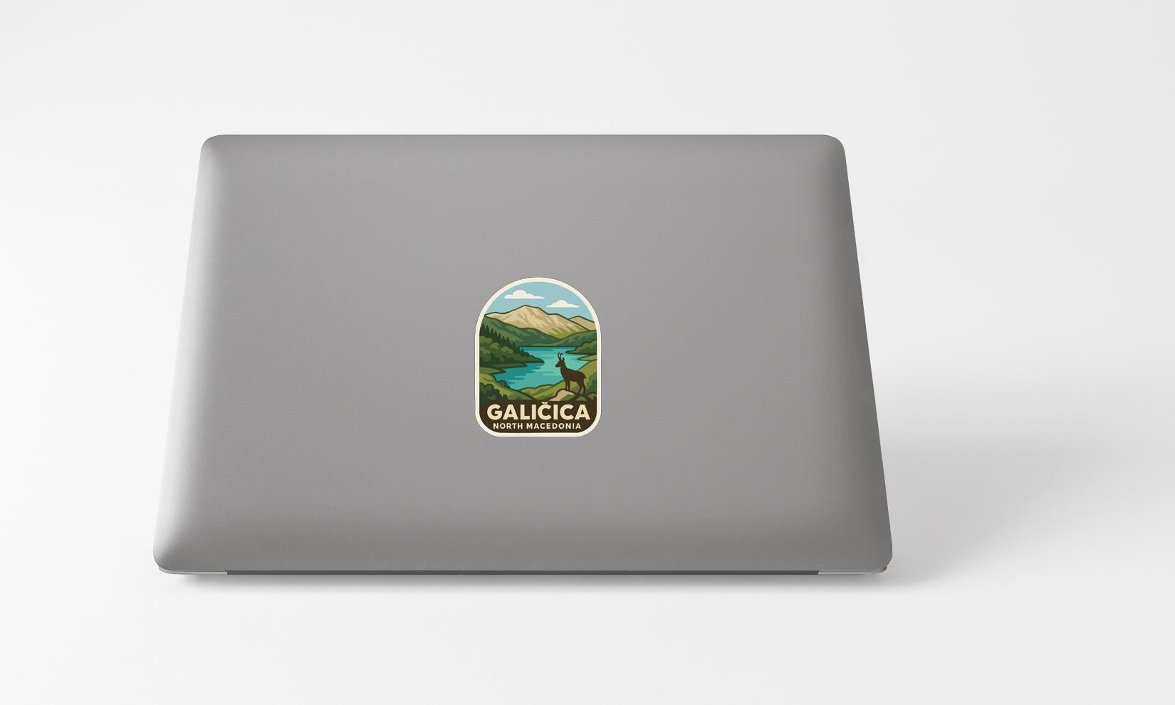 A sticker with a scenic landscape of mountains and a lake is affixed to the back of a laptop computer.