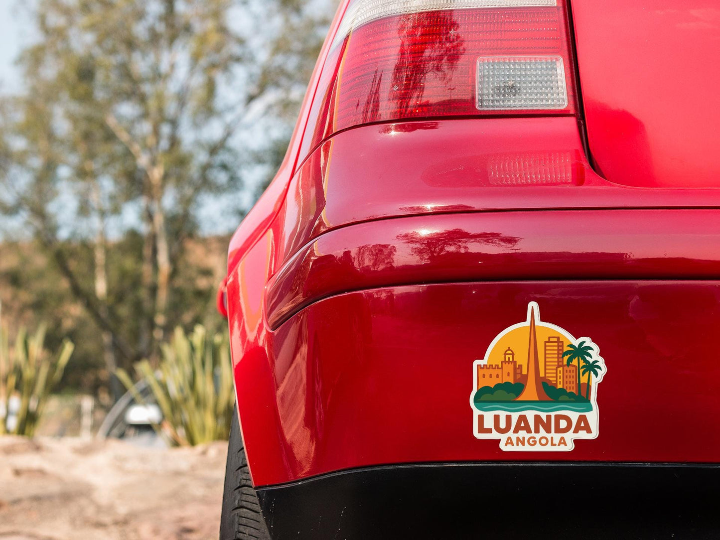 the rear end of a red car with a sticker on the trunk that says "LUANDA ANGOLA".