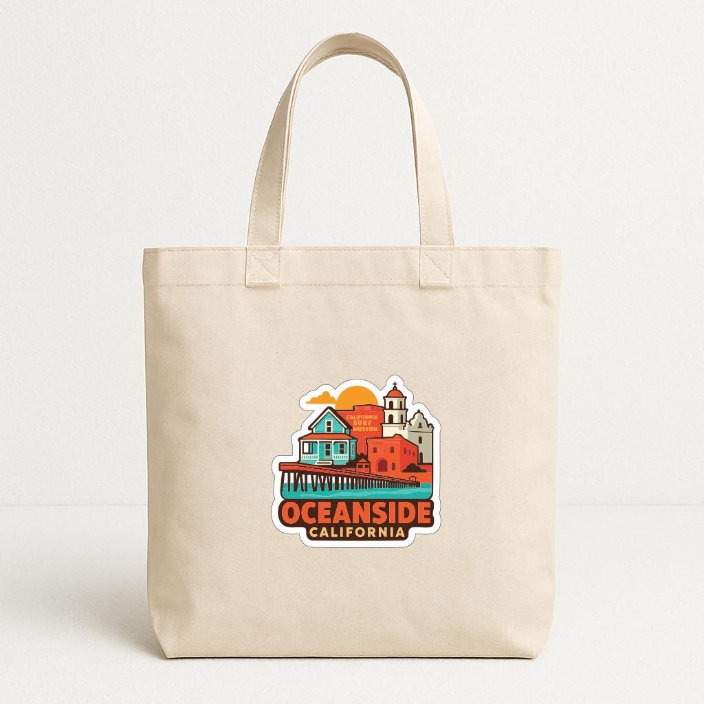 A beige tote bag with a printed design depicting a coastal city scene with a pier and buildings, along with the text "OCEAN SIDE CALIFORNIA".