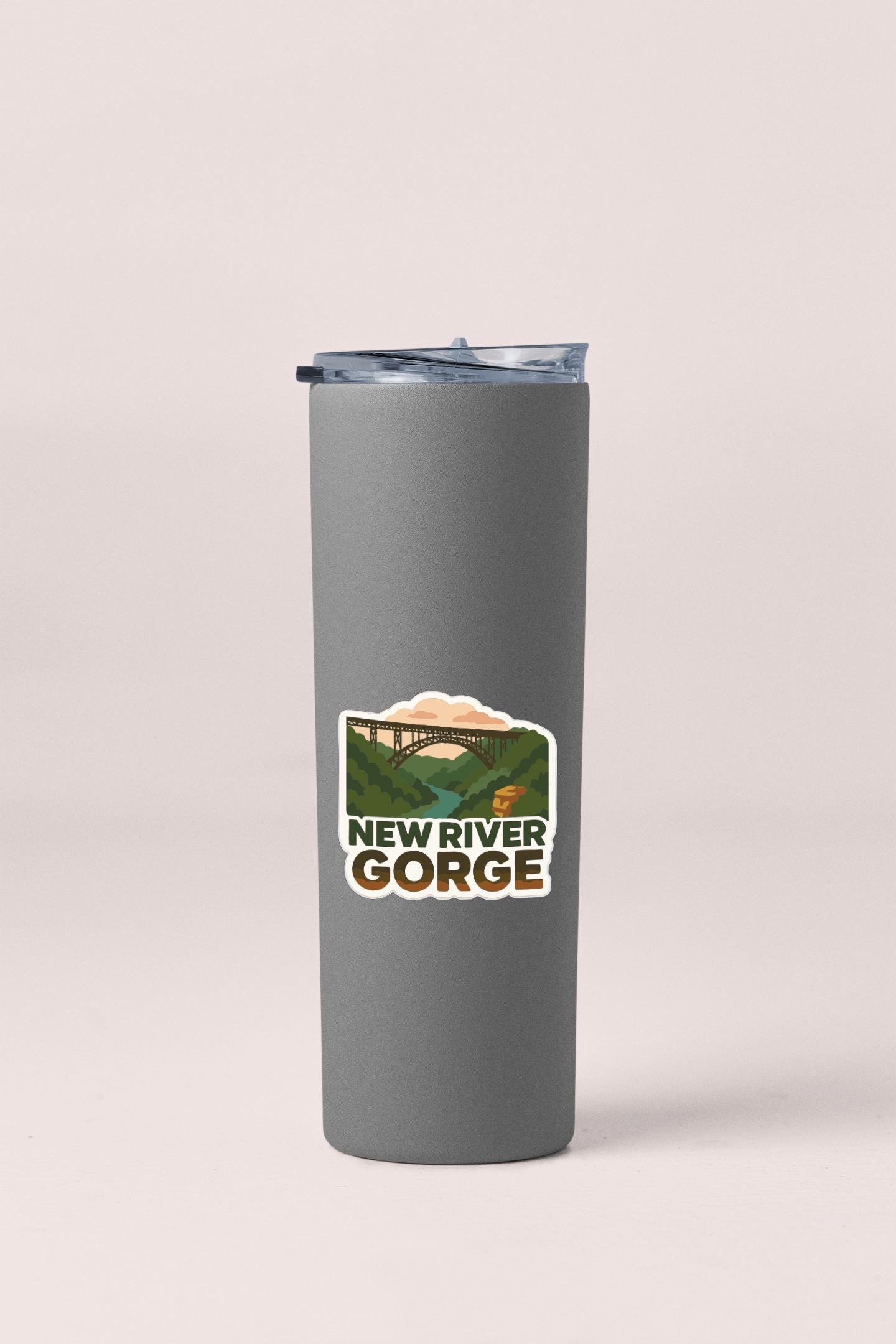 A gray insulated tumbler with a lid and a sticker depicting the New River Gorge.
