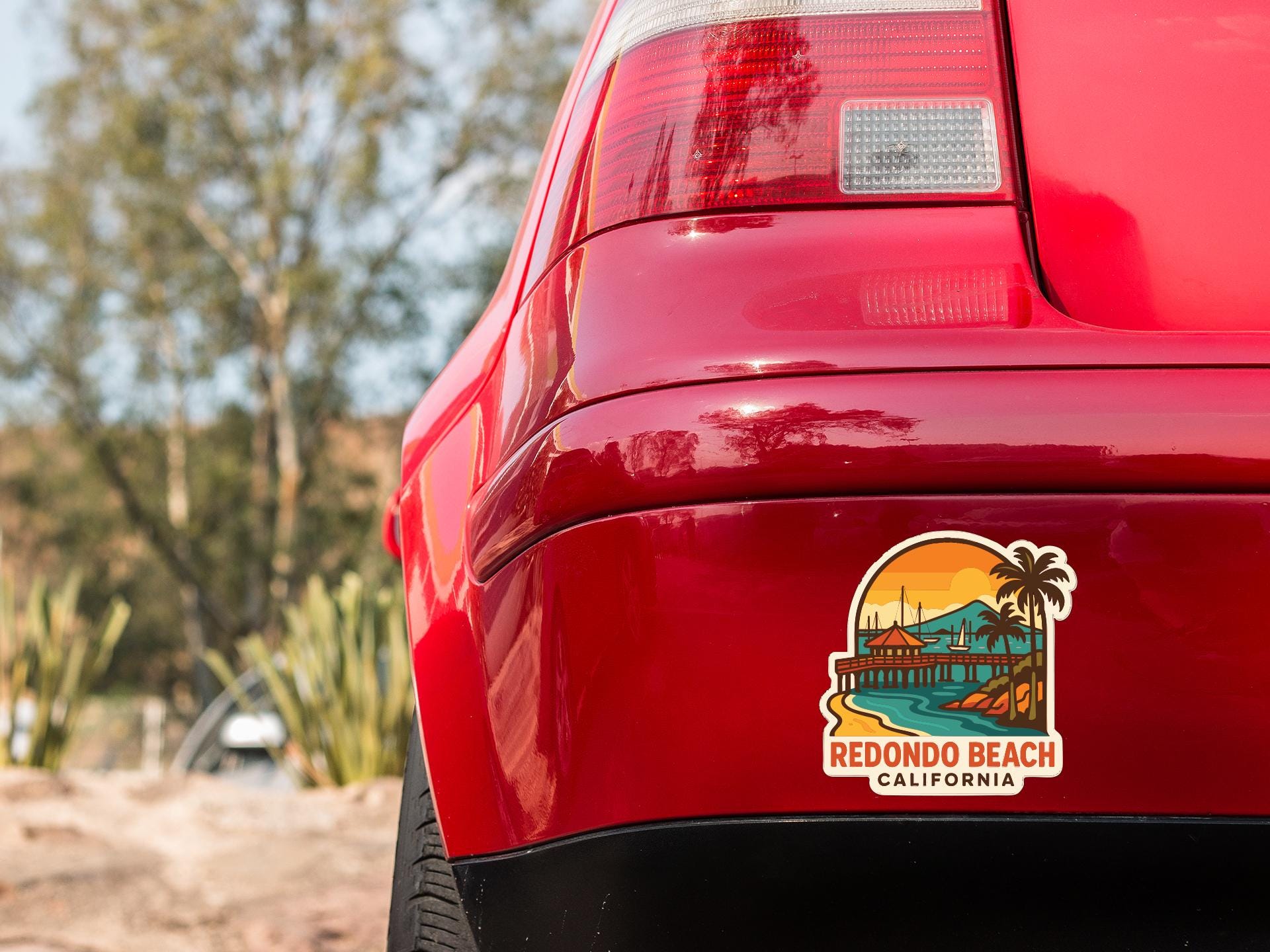 the rear end of a red car with a sticker on the trunk that says "Redondo Beach, California".