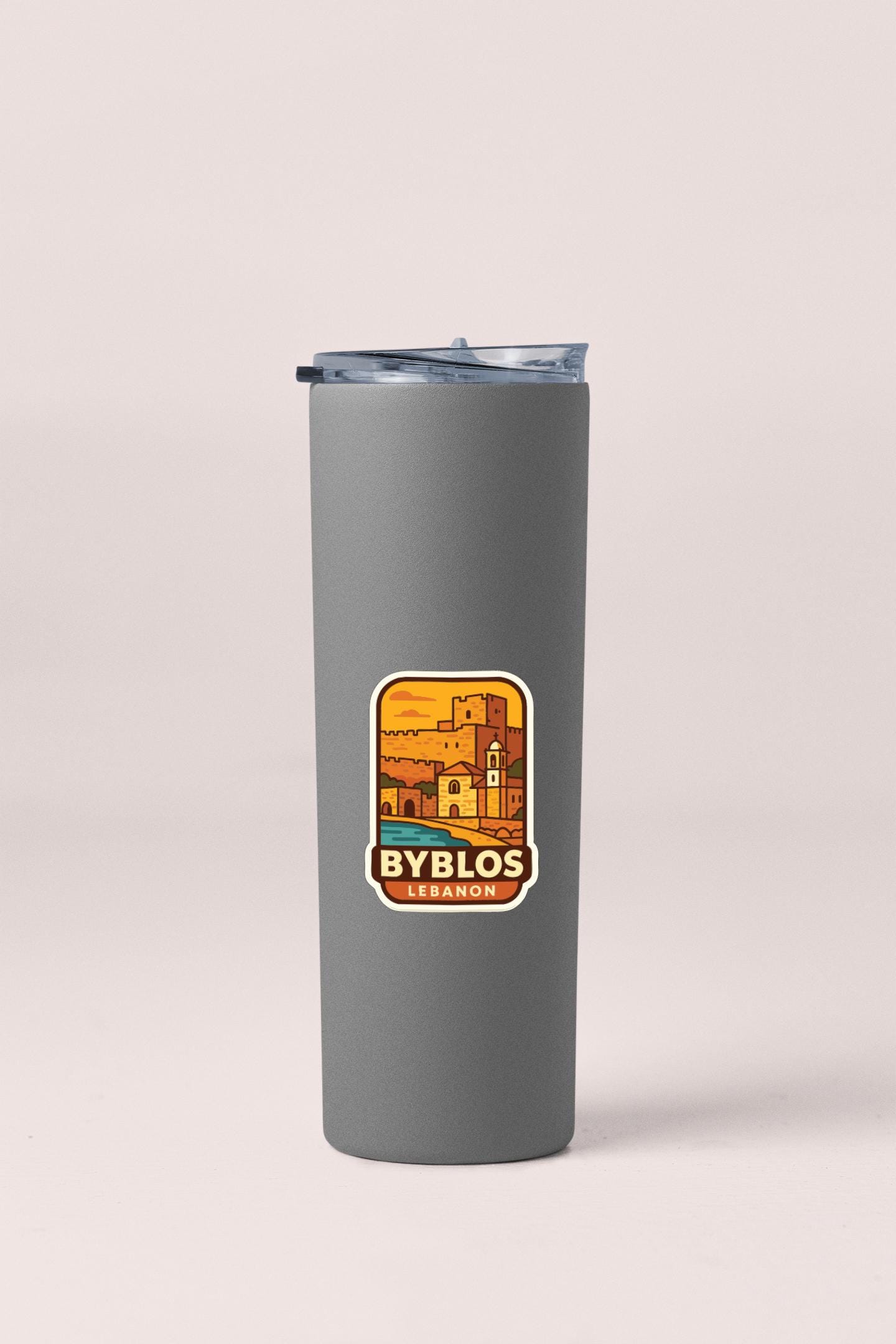 A gray insulated tumbler with a sticker featuring an illustration of a building and the text "BYBLOS" and "LEBANON".