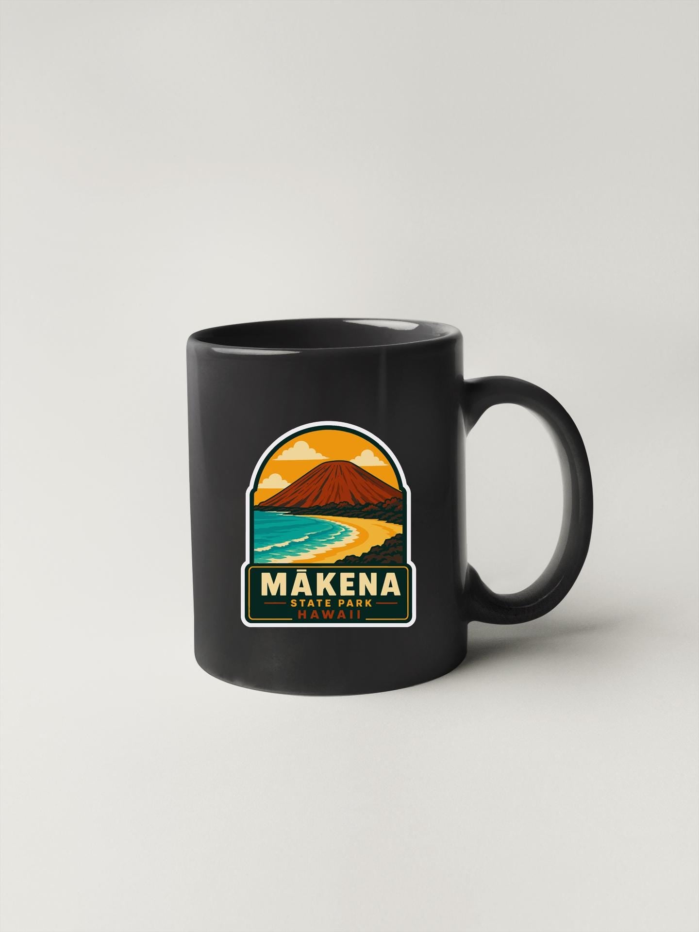 A black coffee mug with a graphic design depicting a mountain landscape and the text "MAKENA STATE PARK, HAWAII" printed on it.