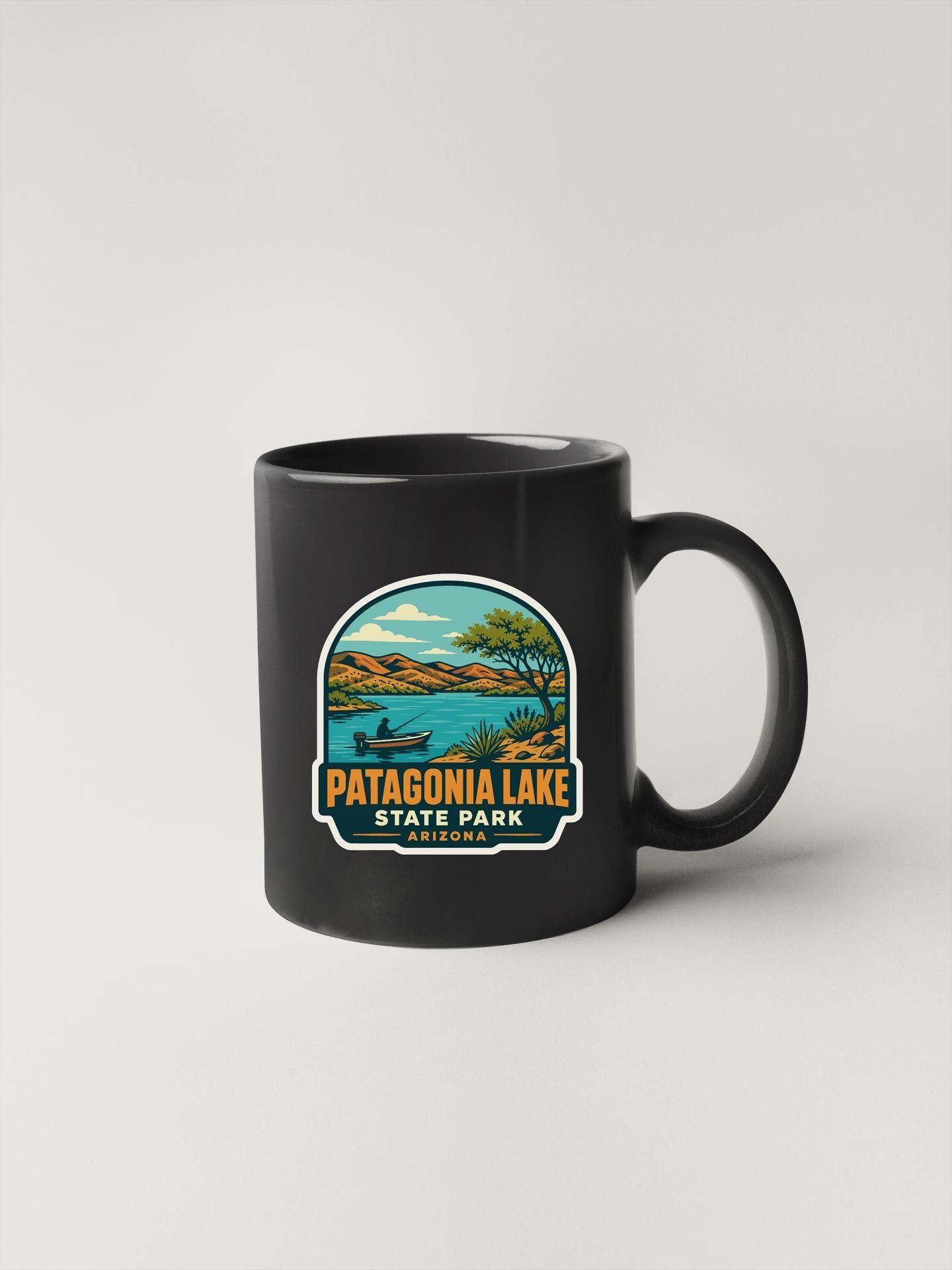 A black coffee mug with a graphic design depicting Patagonia Lake and the surrounding landscape.