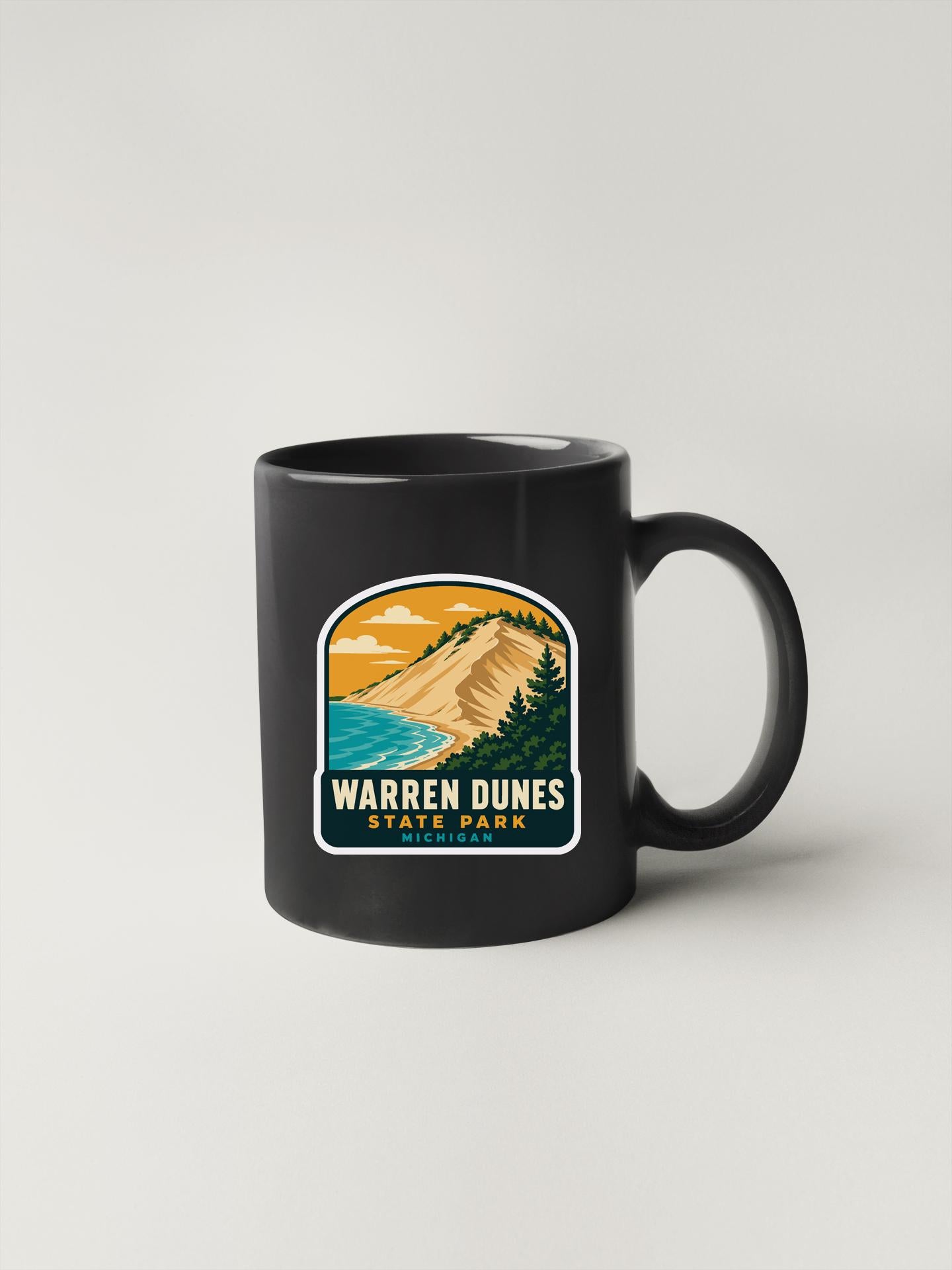 A black coffee mug with a graphic design depicting a scenic landscape, including mountains, a beach, and a body of water.