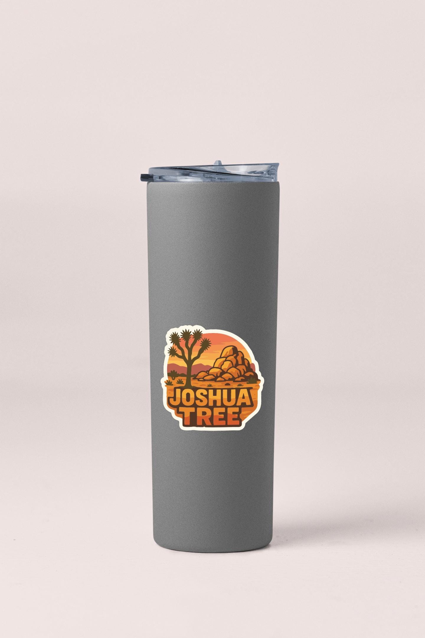 A gray insulated tumbler with a sticker featuring an illustration of a desert landscape.