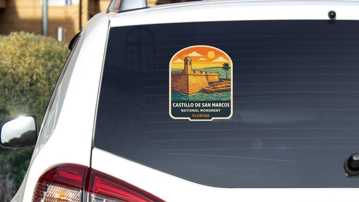 A sticker on the rear window of a white car, depicting a scenic view of Castillo de San Marcos National Monument in Florida.