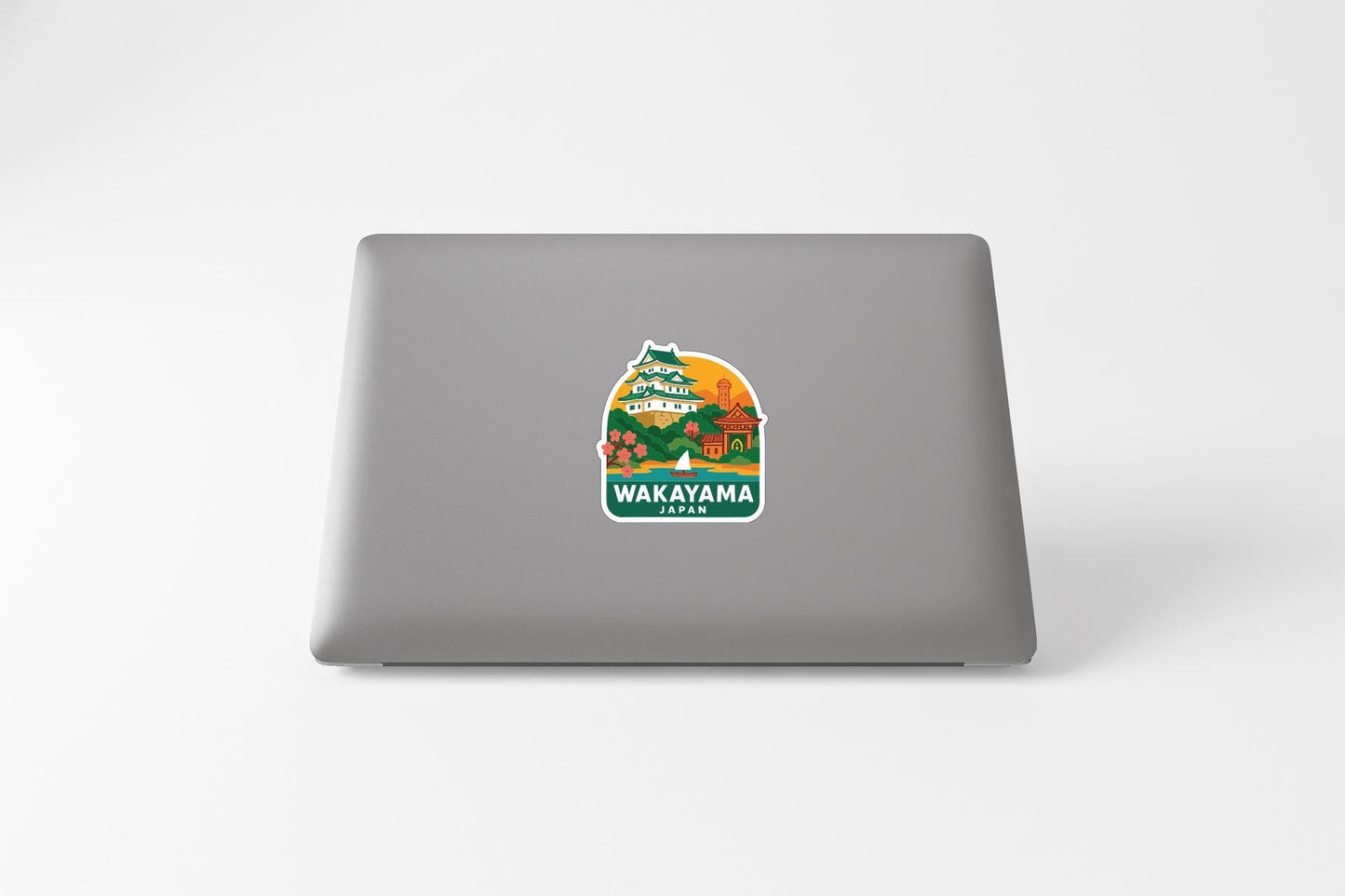 A sticker on the back of a laptop, depicting a scenic landscape with a large orange sun and various elements such as trees, buildings, and mountains.