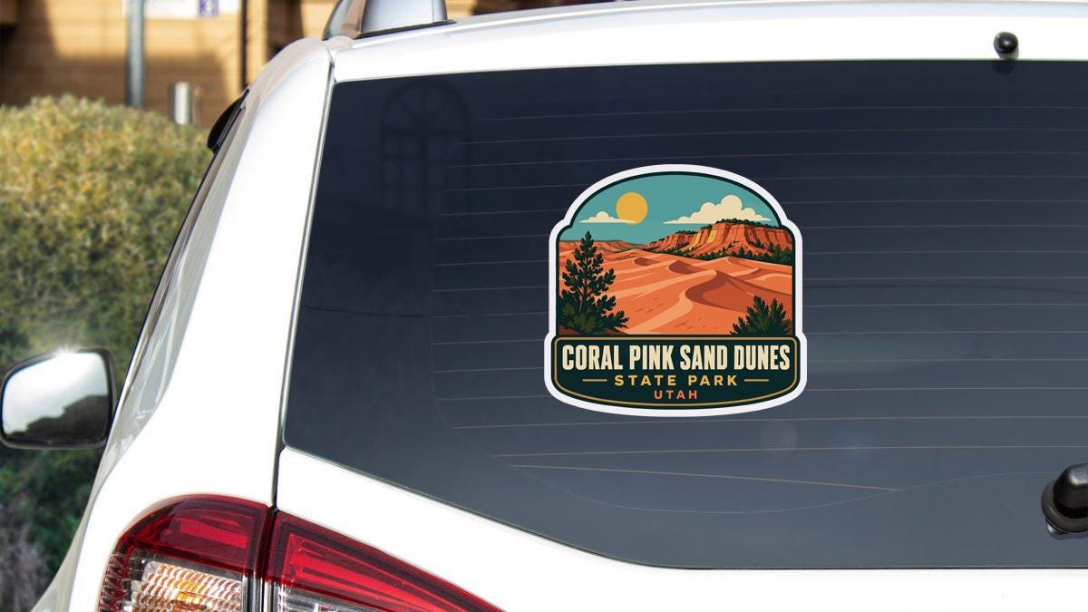 A sticker on the rear window of a car that says "Coral Pink Sand Dunes State Park Utah".