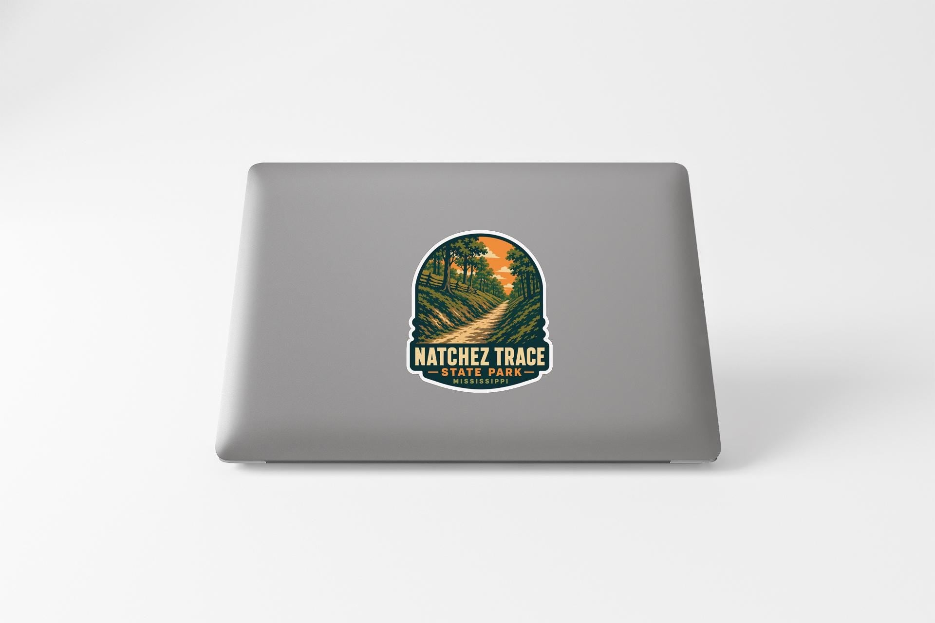 A sticker on the back of a laptop, depicting a scenic landscape with a winding path and trees.