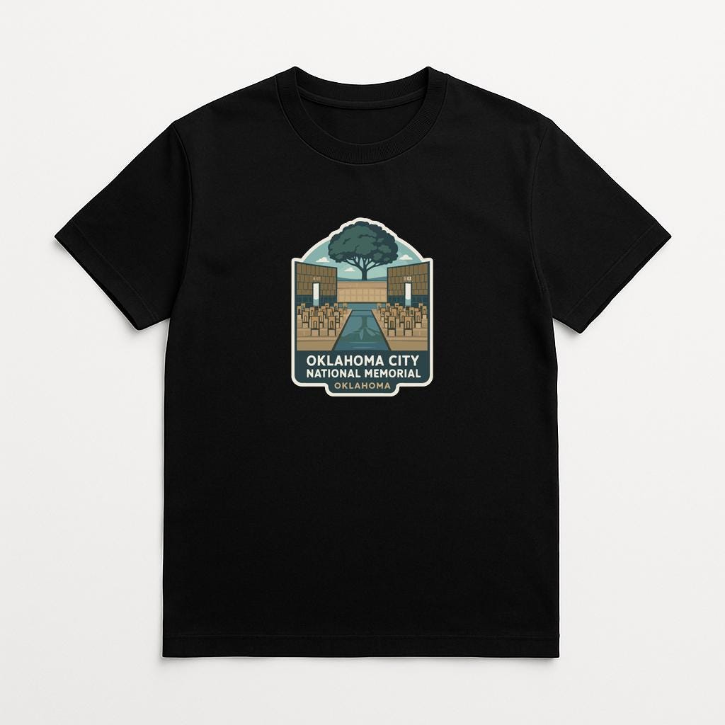 A black t-shirt with a graphic design depicting a tree and a building, along with the text "OKLAHOMA CITY NATIONAL HISTORY" printed on it.