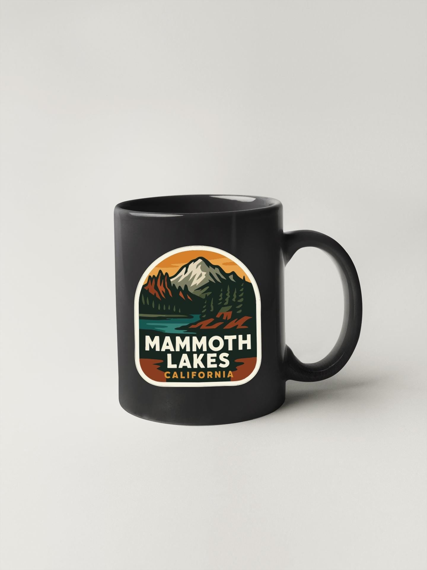 A black coffee mug with a graphic design featuring a mountain landscape and the text "Mammoth Lakes California".