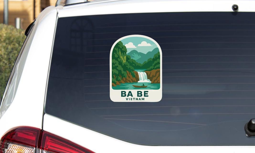 A sticker on the rear window of a car, depicting a scenic landscape with a waterfall and mountains.