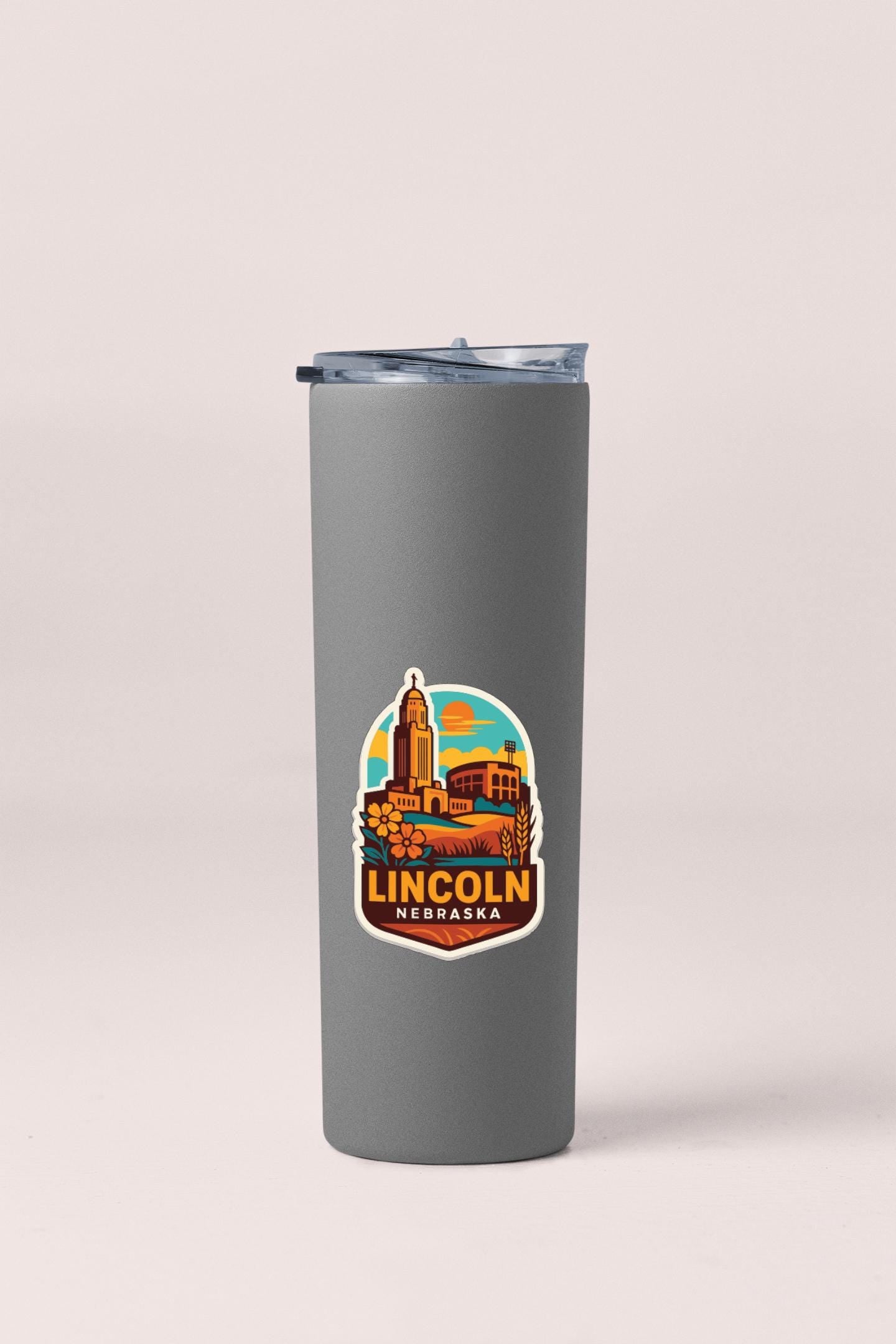 A gray insulated tumbler with a colorful sticker depicting a cityscape and the text "LINCOLN NEBRASKA" printed on it.