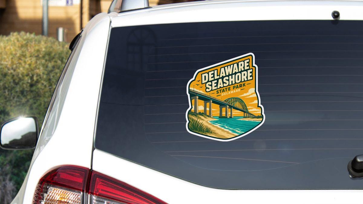 A sticker on the rear window of a white car, depicting a scenic view of Delaware Shore State Park.
