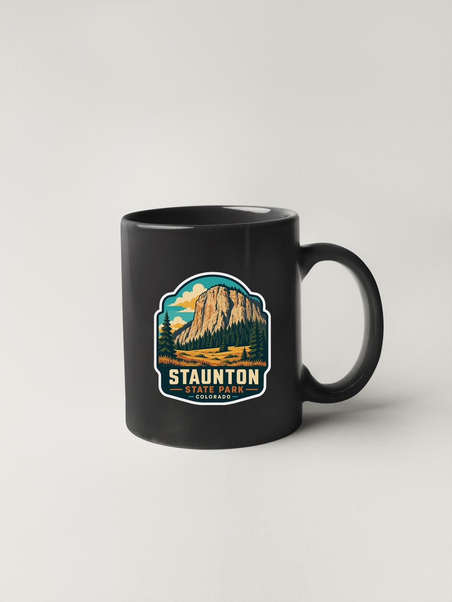 A black coffee mug with a graphic design depicting Staunton State Park in Colorado.
