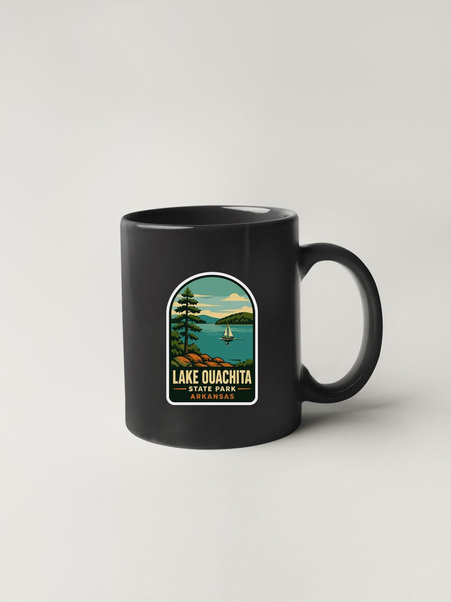 A black coffee mug with a sticker depicting Lake Quachita State Park in Arkansas.