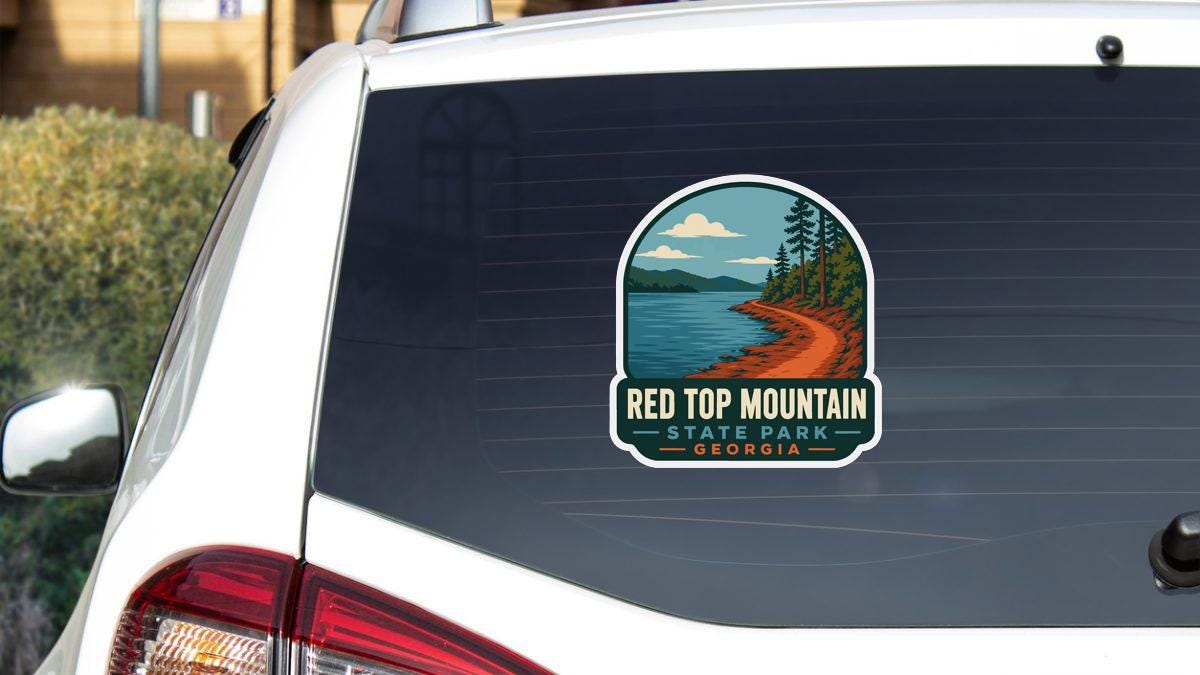 A sticker on the rear window of a white car, depicting a scenic landscape with a river, mountains, and pine trees.