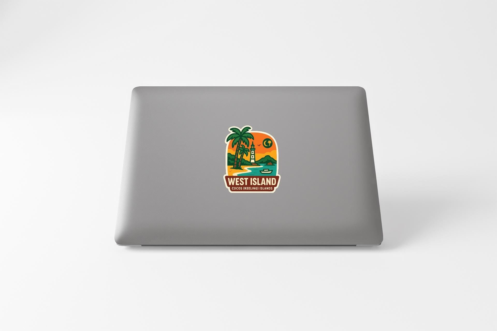 A sticker on the back of a laptop, depicting a tropical island scene with palm trees, a sunset, and a house.