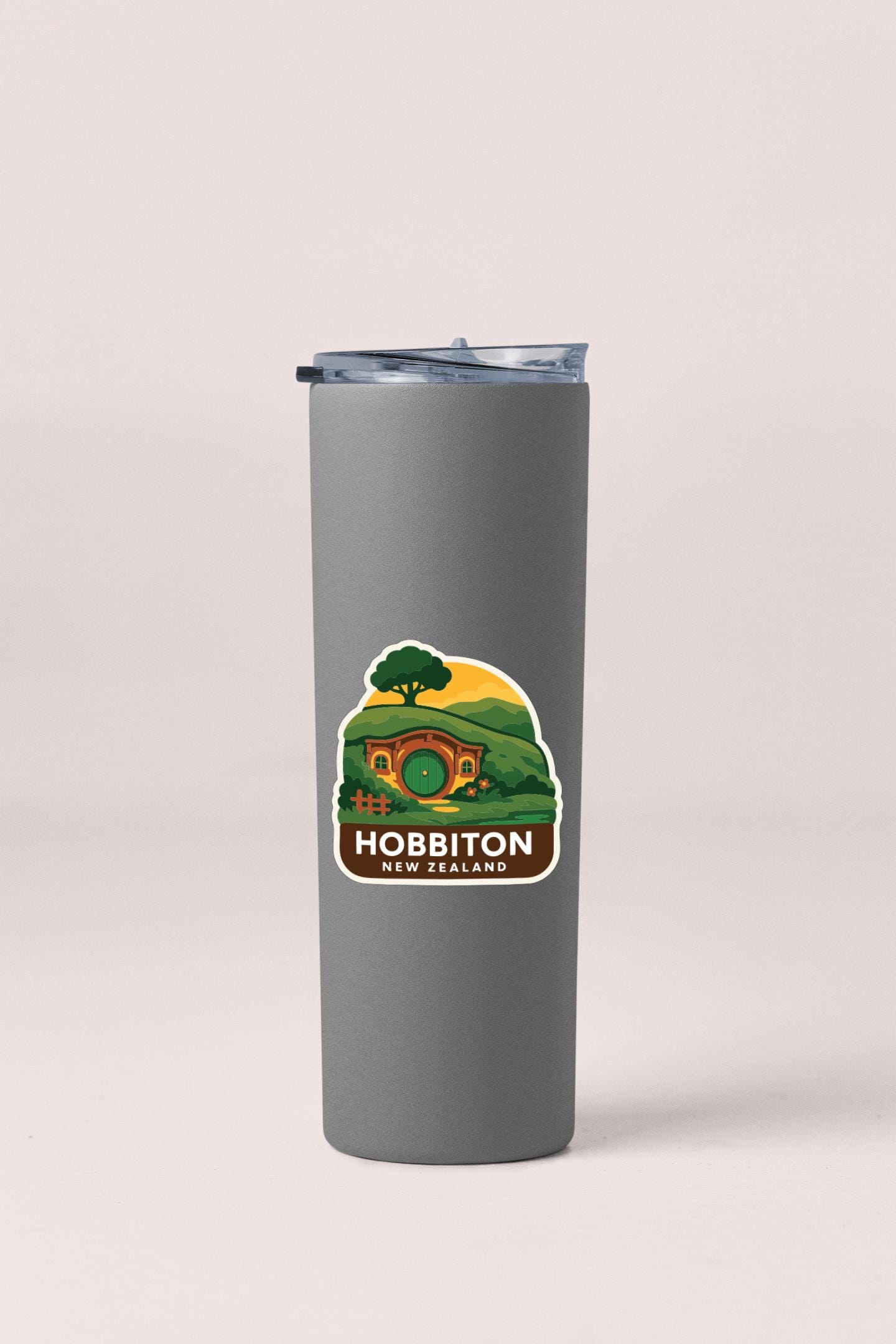 A gray tumbler with a sticker depicting a landscape and the text "HOBBITON NEW ZEALAND".