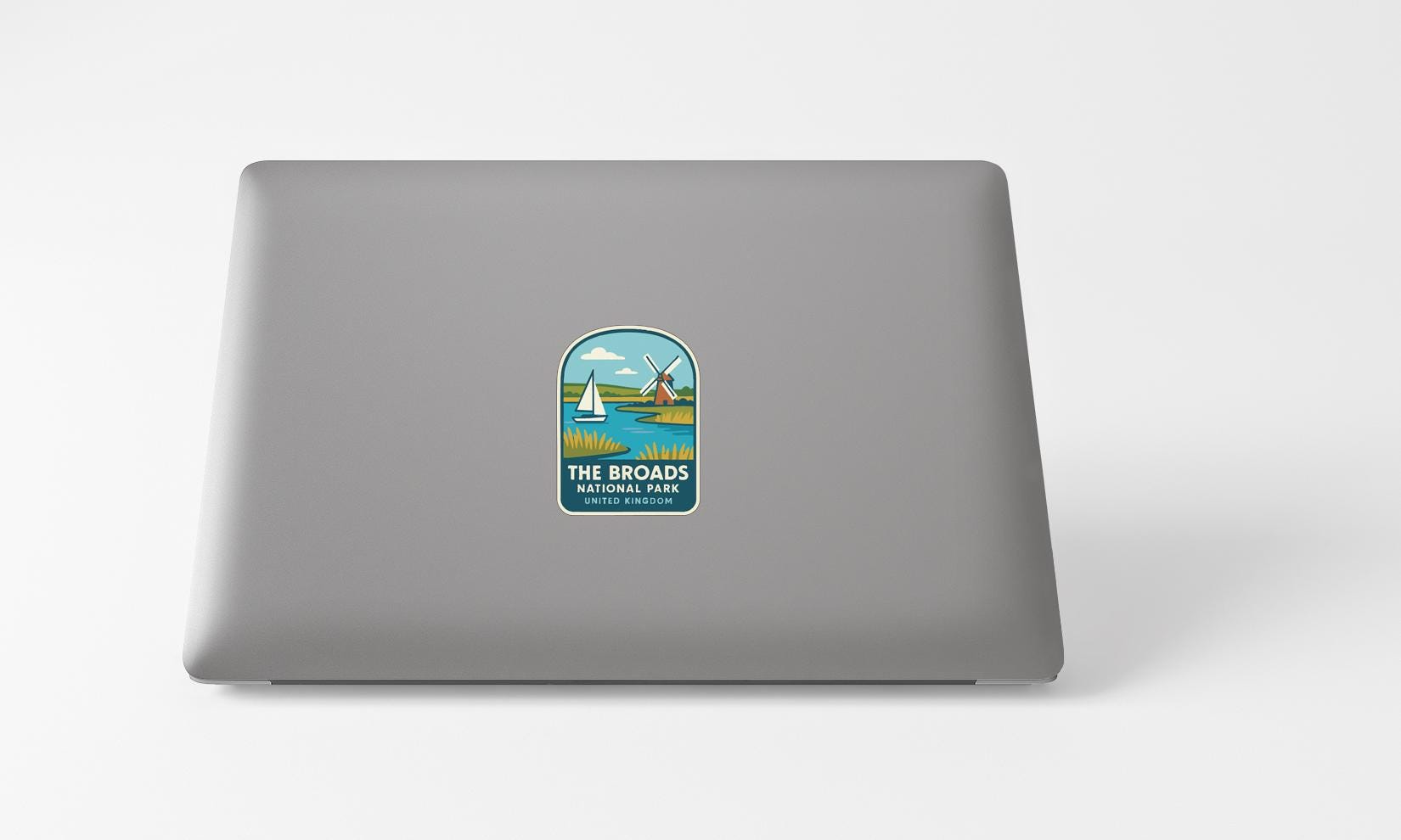a sticker on the back of a laptop, depicting a sailboat and a landscape with a river.