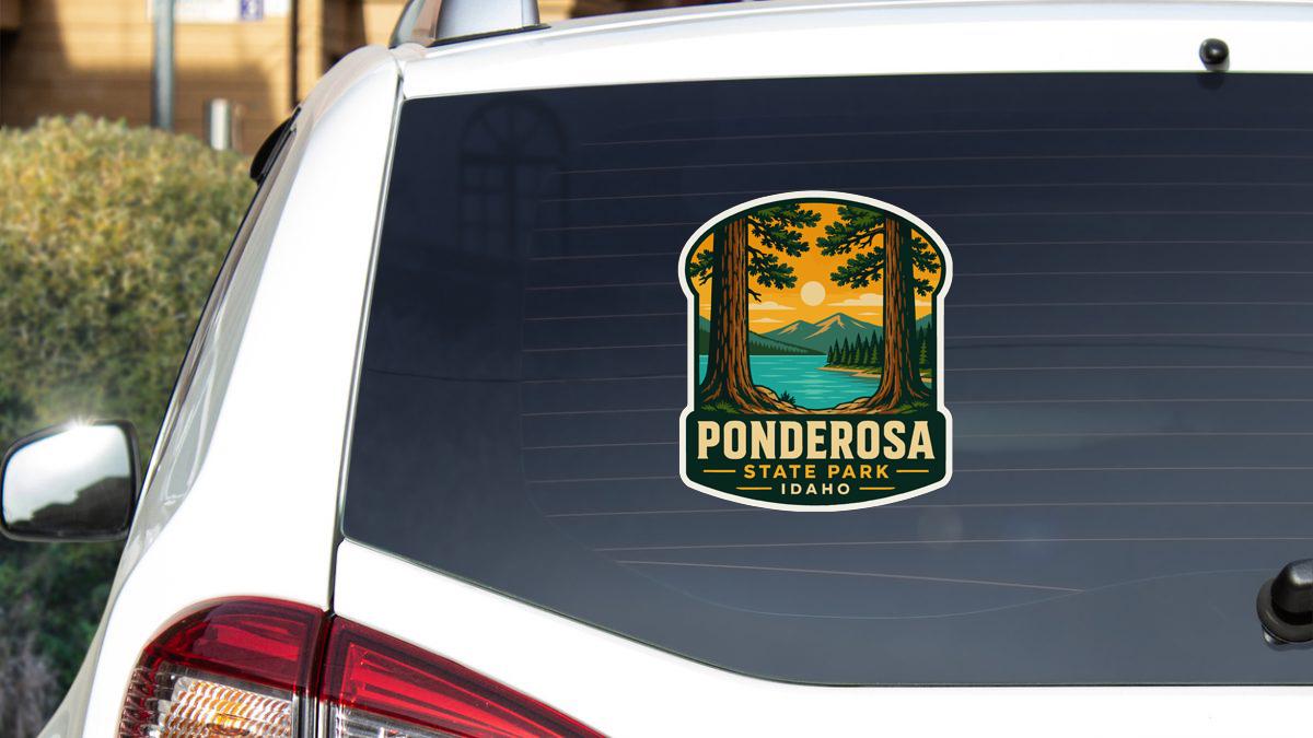 A sticker on the rear window of a white car, depicting a scenic landscape with trees, mountains, and a sunset.