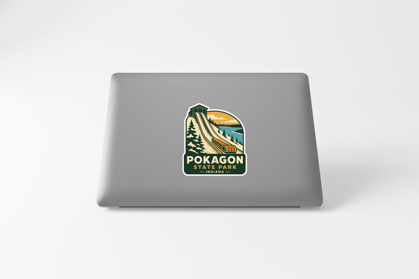 A sticker on the back of a laptop, depicting a scenic landscape with mountains, trees, and a winding road.