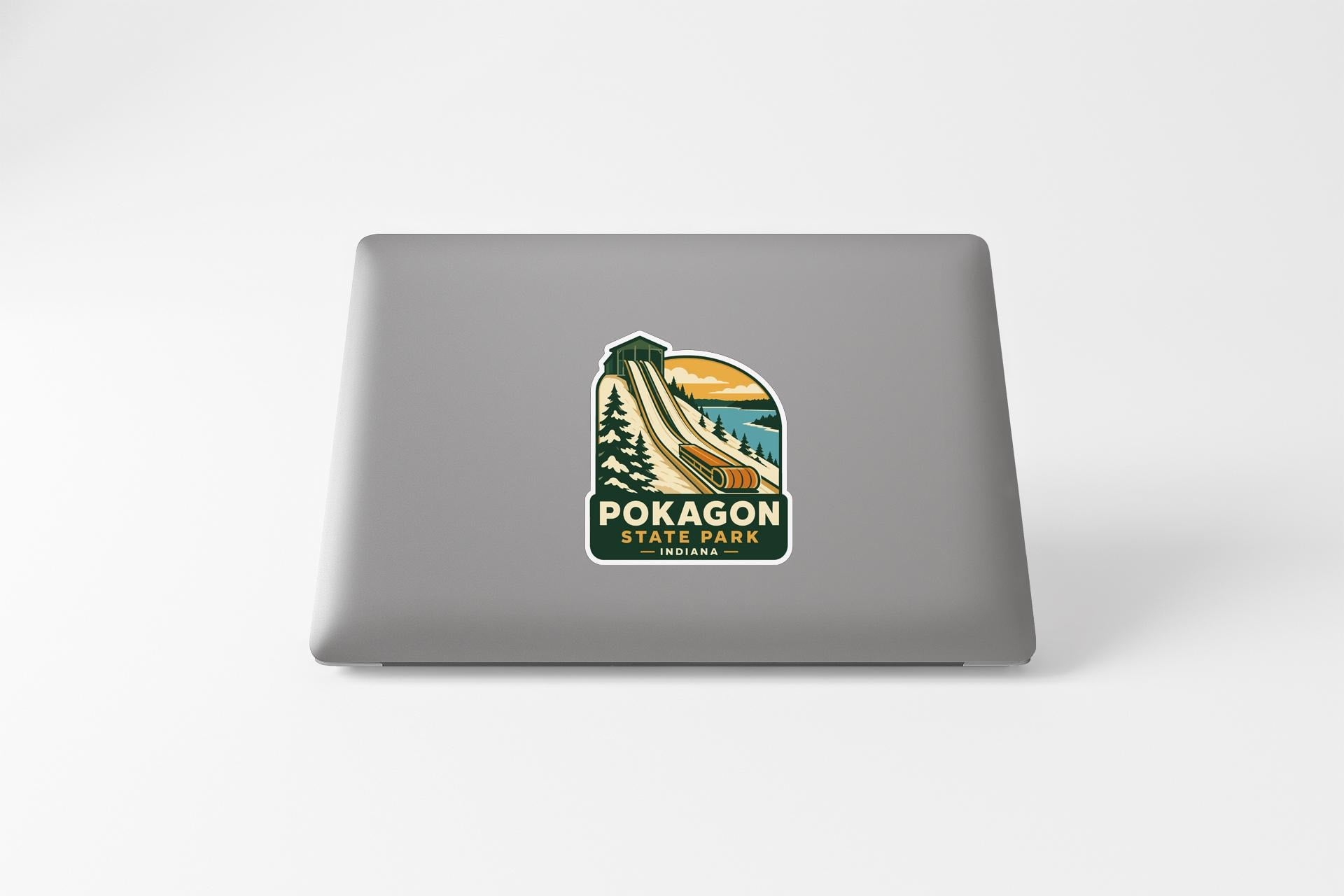 A sticker on the back of a laptop, depicting a scenic landscape with mountains, trees, and a winding road.