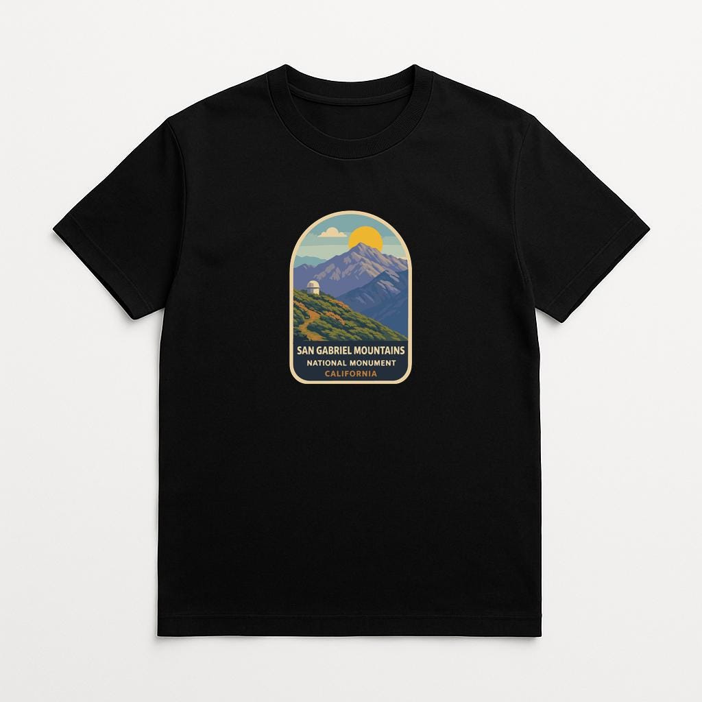 A black t-shirt with a graphic design depicting a mountain landscape with a yellow sun in the sky.
