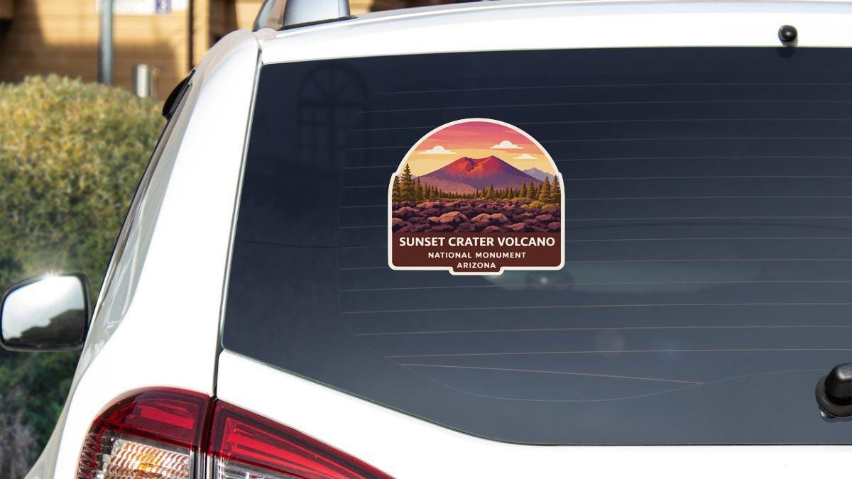 A sticker on the rear window of a white car, depicting a scenic landscape with a mountain and a sunset.