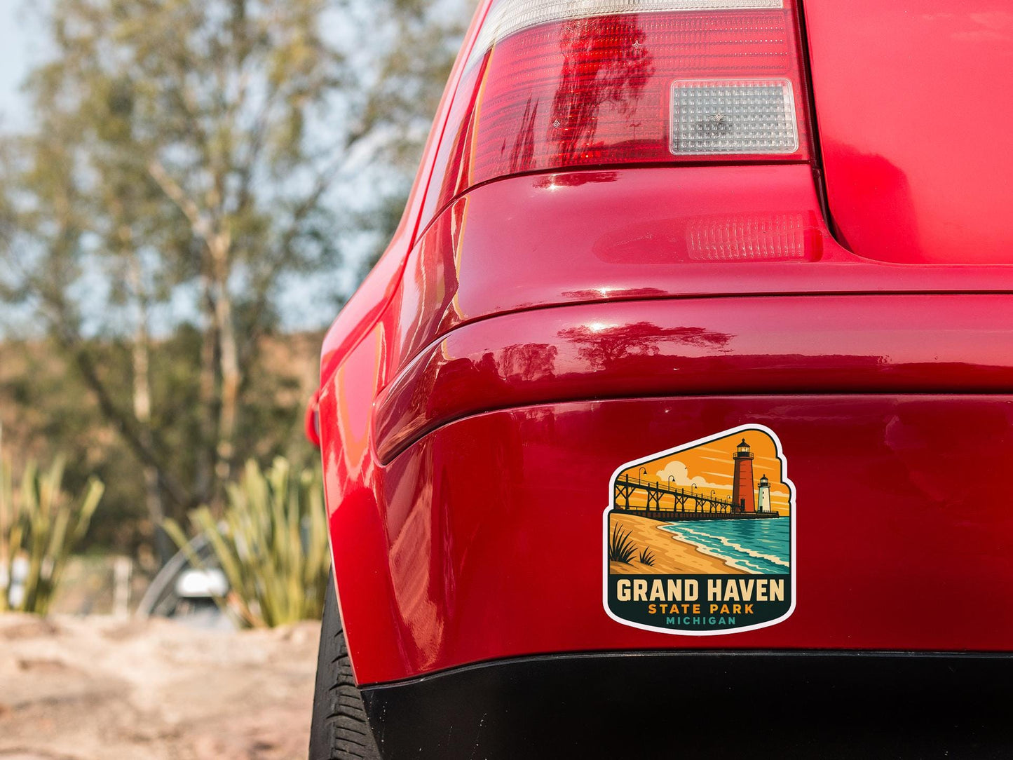 the rear end of a red car with a sticker on the back window that says "Grand Haven State Park, Michigan".