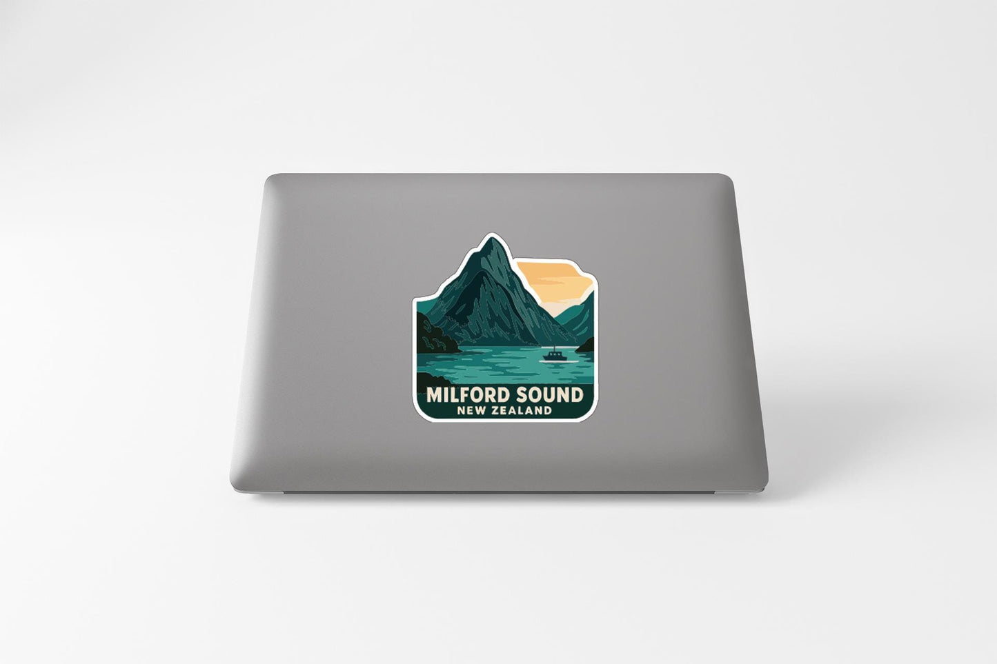 a sticker on the back of a laptop that displays a mountain landscape with a lake and a boat, along with the text "MILFORD SOUND NEW ZEALAND".