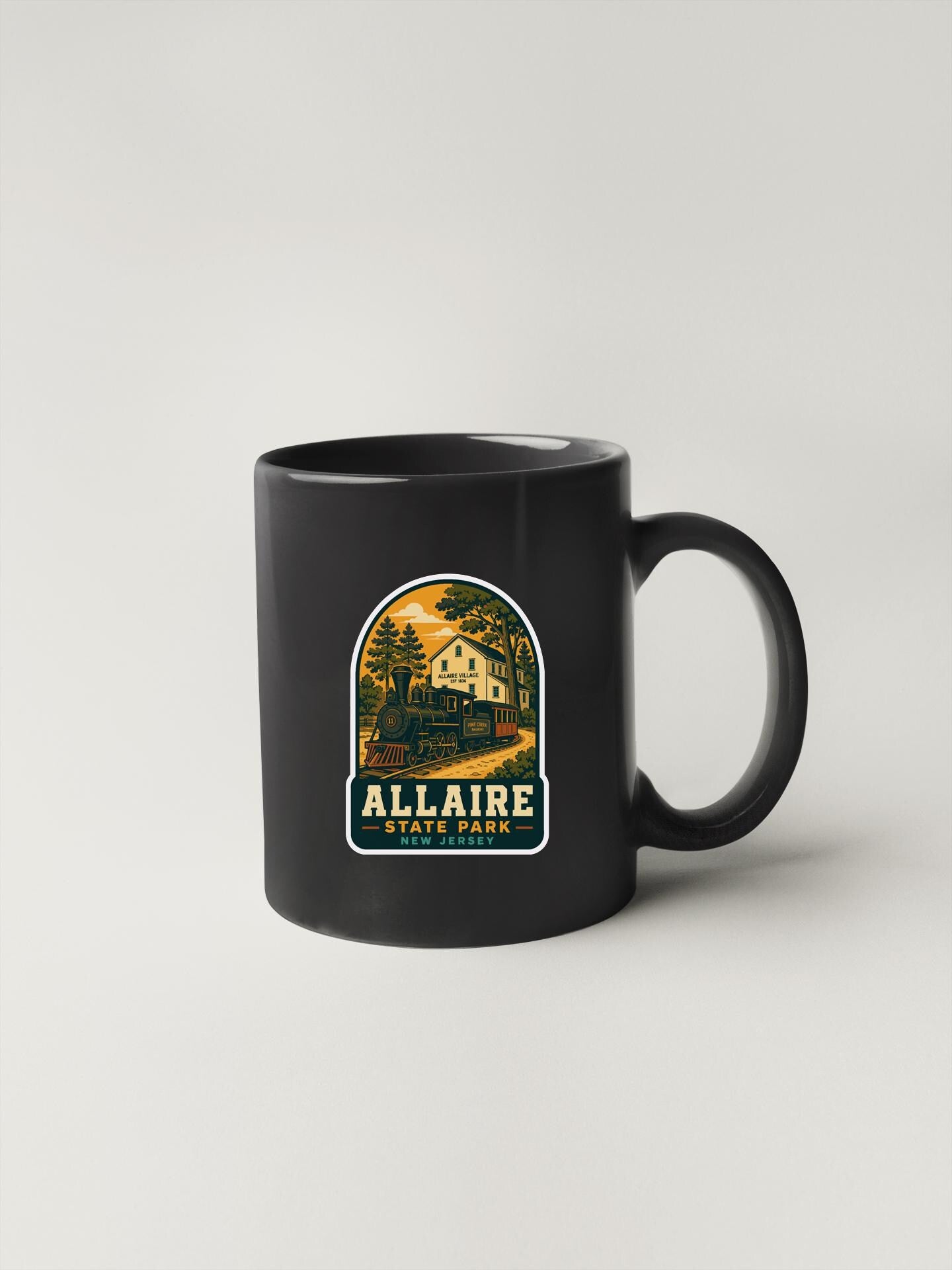 A black coffee mug with a sticker depicting a scenic landscape and the text "Allaire State Park" printed on it.