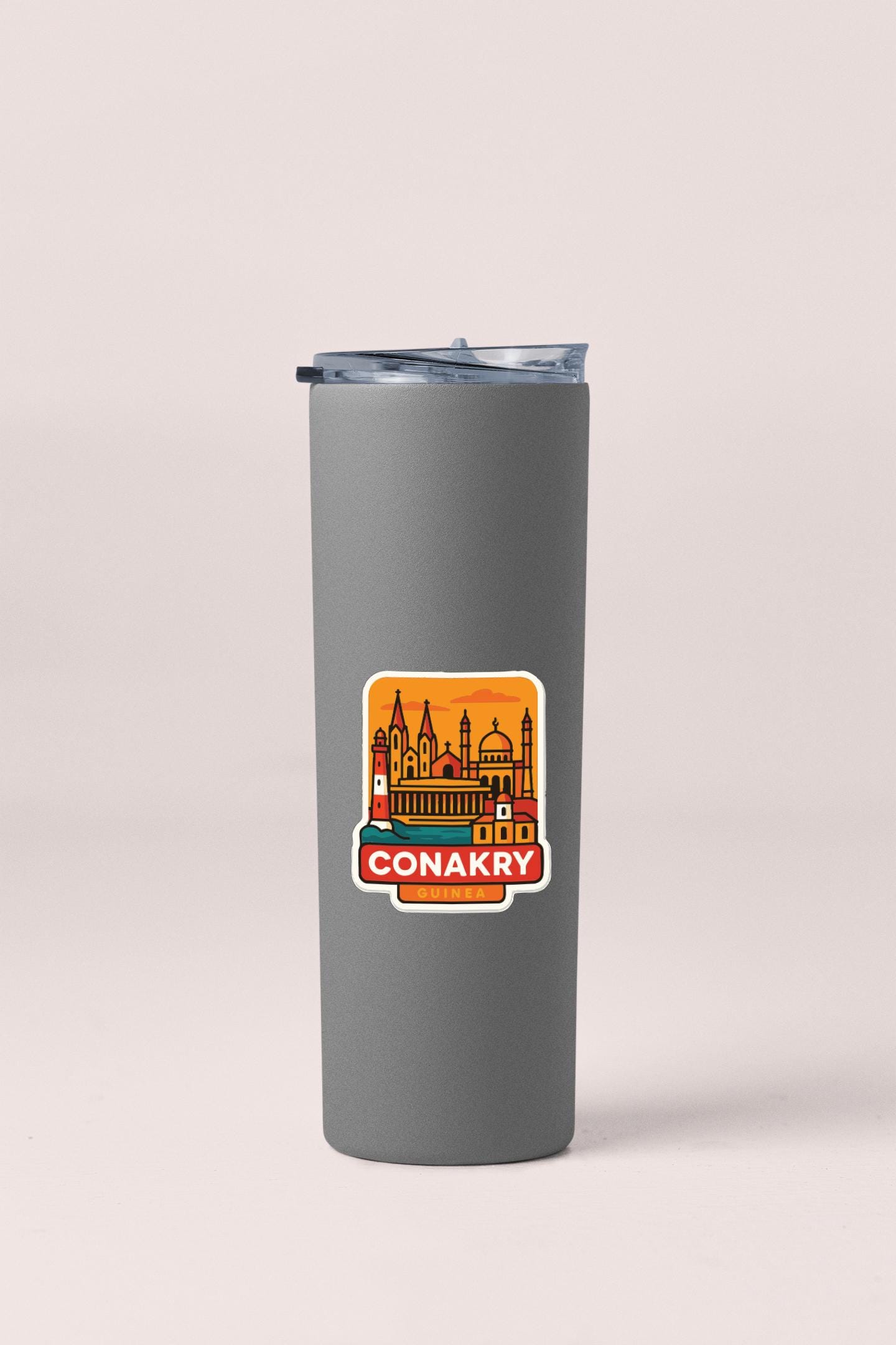 A gray insulated tumbler with a sticker depicting the Conakry skyline.