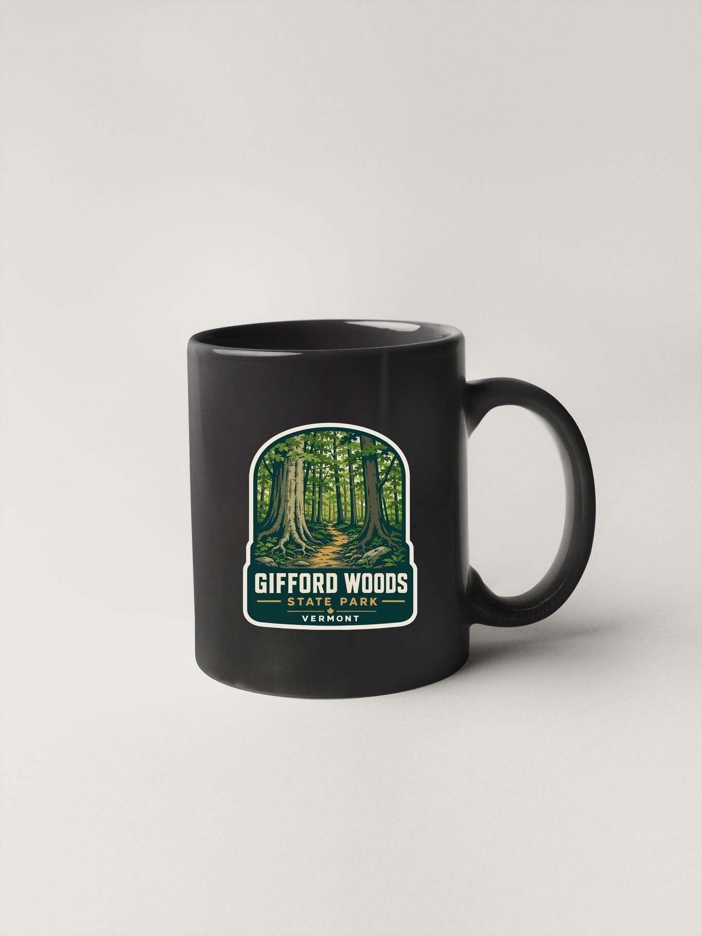 A black coffee mug with a sticker depicting a forest scene and the text "Gifford Woods State Park Vermont".