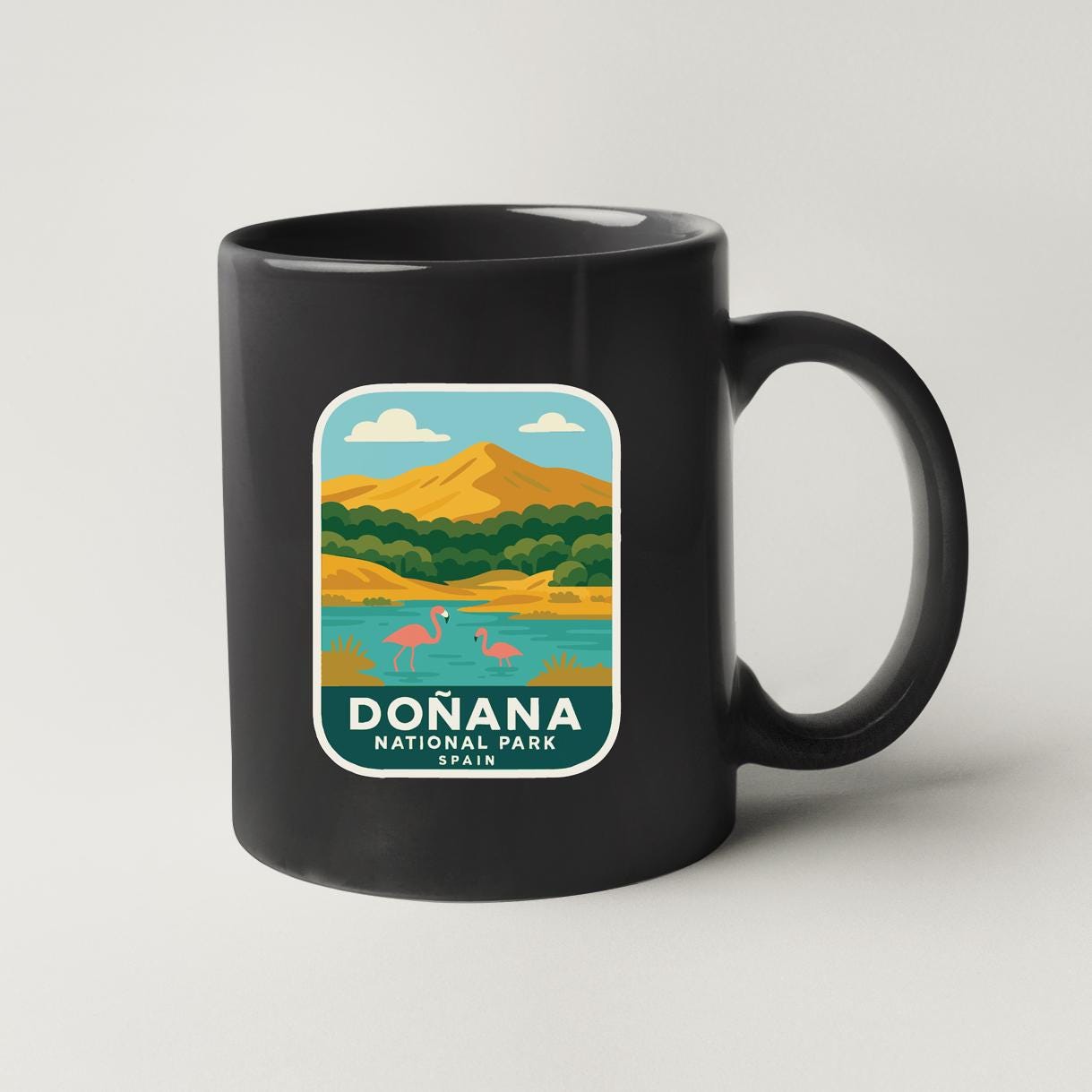 A black coffee mug with a colorful graphic depicting a scenic landscape with mountains, a lake, and flamingos.