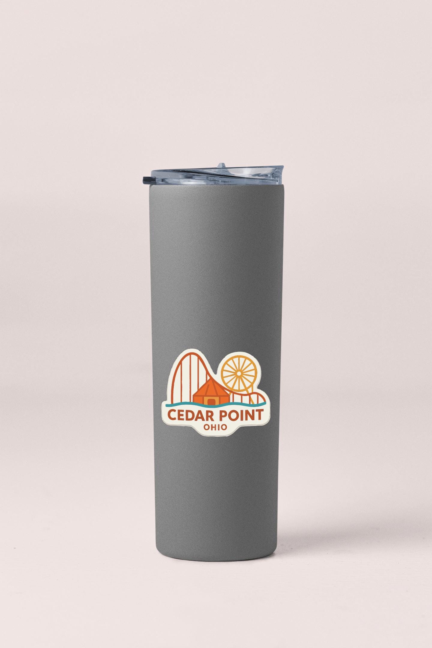 A gray insulated tumbler with a lid and a sticker featuring an illustration of a roller coaster and the text "Cedar Point, Ohio".