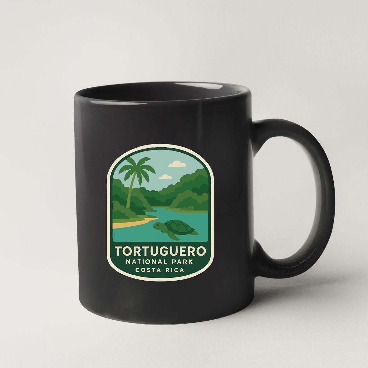 A black coffee mug with a graphic design depicting a tropical landscape, including a palm tree, river, and mountains.