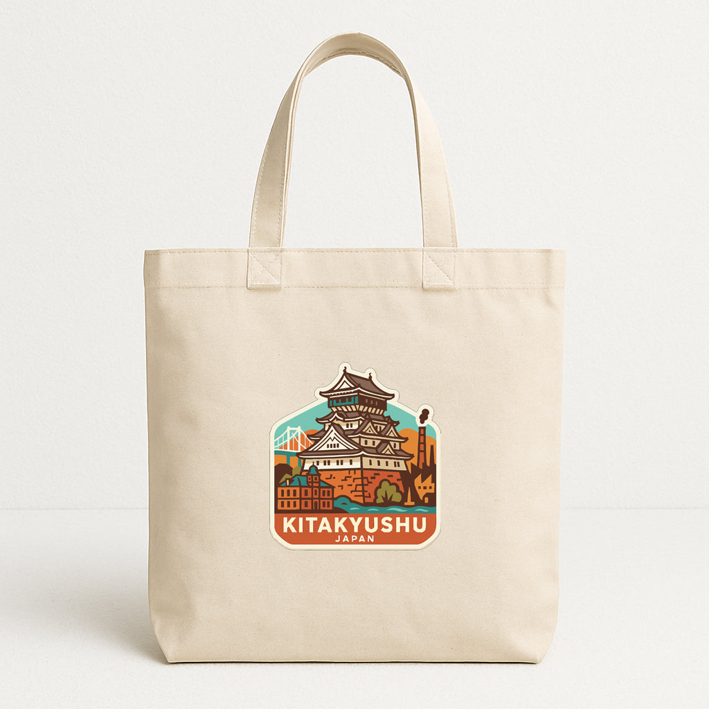 A beige tote bag with a printed design of a castle or palace-like structure, along with the text "KITAKYUSHU JAPAN" printed on it.
