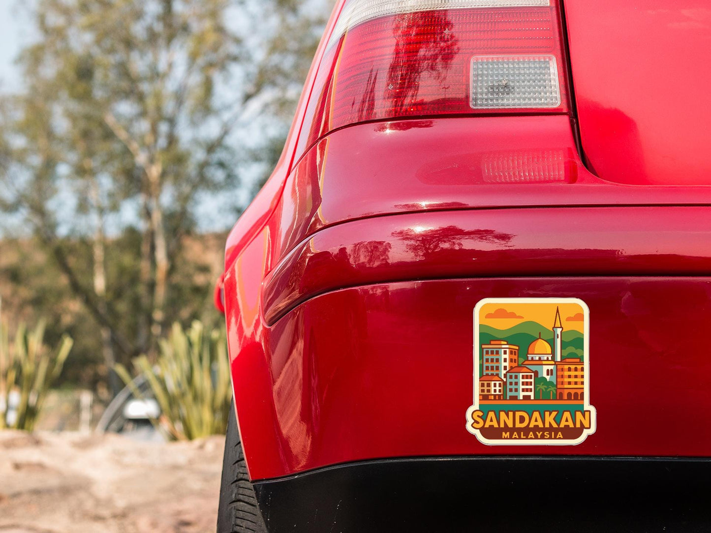 the rear end of a red car with a sticker on the trunk that says "Sandakan Malaysia".