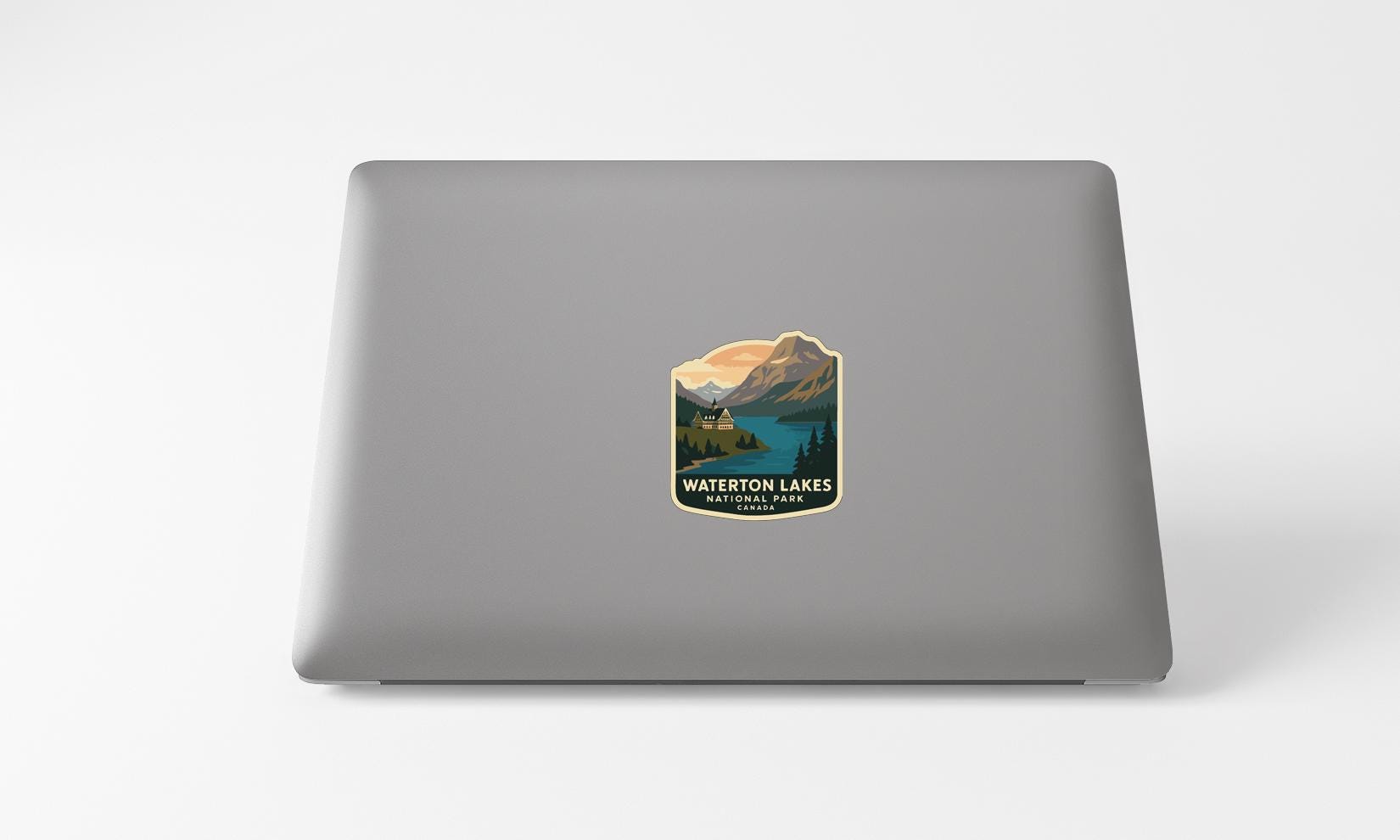 A sticker on the back of a laptop, depicting a scenic landscape with mountains, a lake, and a cabin.