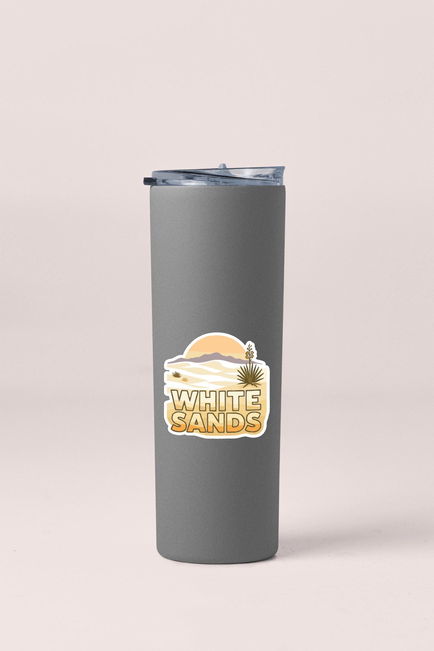 A gray insulated tumbler with a lid and a sticker featuring a desert landscape and the text "WHITE SAND".